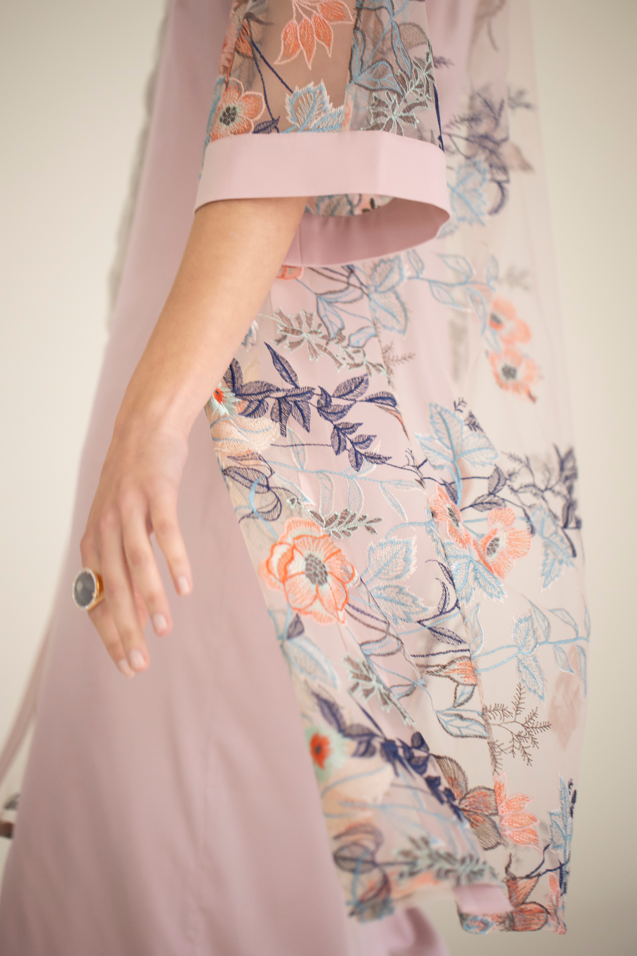 Vestido largo de seda naranja en percha junto a la ventana, con rollos de tejidos naturales